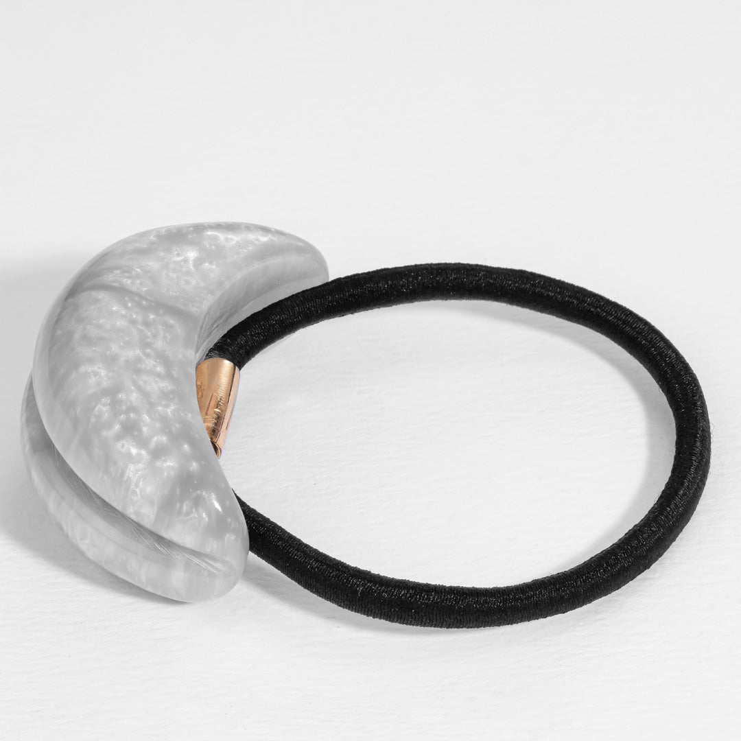 Black hair tie with textured gray holder on a light gray background